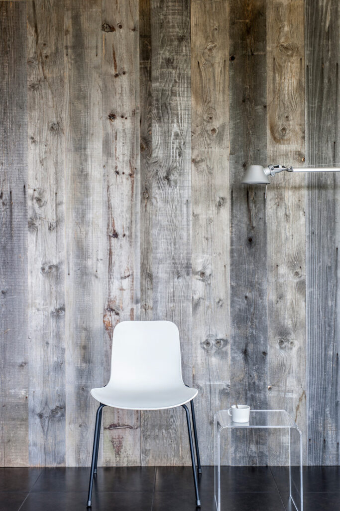 Presentatie van grijze barnwood wandbekleding met witte stoel en lamp
