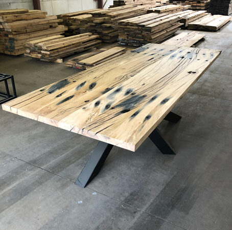 Presentatie van een tafel van geschaafde eiken spoorbielsplanken met zwart stalen kruispoot en tekening in oud hout loods